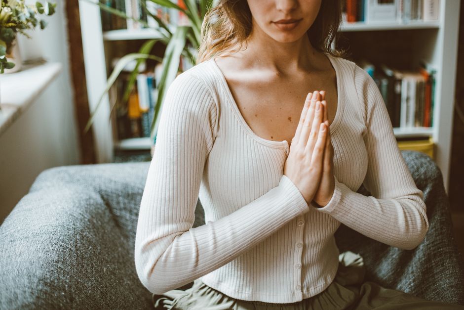 A woman practicing meditation indoors, focusing with hands in prayer position.